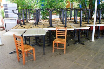Fototapeta na wymiar Tables and chairs stacked outside closed cafe-restaurant due the Coronavirus lockdown - Athens, Greece, May 6 2020.