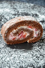 One slice of a homemade chocolate sponge cake roll with strawberries and cream filling, powdered sugar on top, on a slate plate, copy space