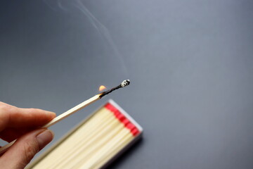Burning match for the fireplace in a woman's hand on a gray background