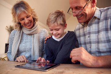Grandson With Grandparents Playing On Digital Tablet At Home Together