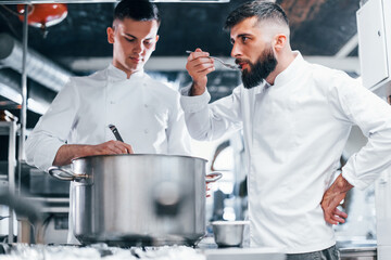 With help from other employee. Chef in white uniform cooking food at kitchen. Busy day at work