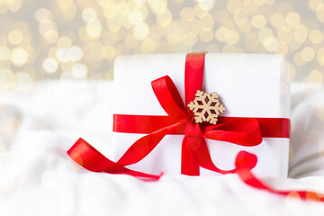 christmas white box with red bow and ribbon gift on soft white blanket with snowflake and bokeh of new year lights. 2021