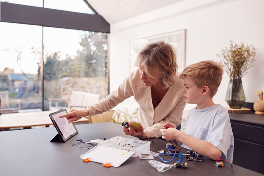 Grandson With Grandmother Assembling Electronic Components To Build Robot Together At Home