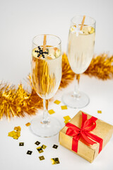 Two glasses with champagne, gold gift box and Christmas decoration with snowflakes on white background