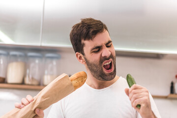 Photo of man biting cucumber and a loaf of bread in her hands.