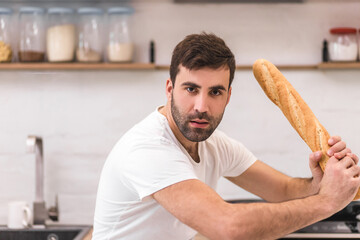 Photo of young handsome man holding whole french baguette on isolated white background.