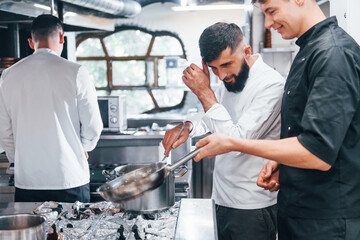 People in white uniform cooking food at kitchen together. Busy day at work
