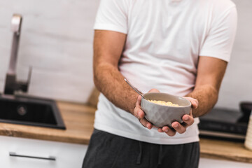 Cropped photo of man holding bowl of cereal with spoon.