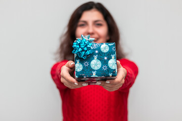 Young smiling woman wearing a red sweater holds a Christmas present in her hands. Happy female with a New Year gift box stands on the with background isolated. Winter holidays concept.