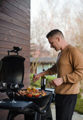 Young smiling man cooks on grill in garden. 