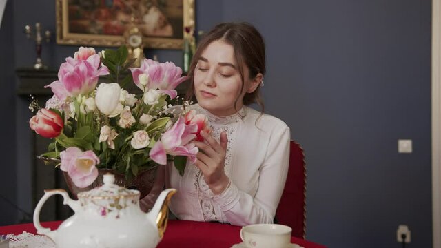 beautiful girl sitting in a room with a vintage interior and enjoys the aroma of fragrant tulips