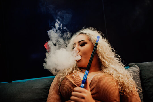 Beautiful Girl smoking hookah in Nightclub. Exhaling smoke. Sexy girl smokes hookah.Sexy brunette vaping hookah or shisha
