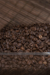 Perspective view on coffee beans in a plastic transparent box on a wooden table. Fresh medium roasted coffee beans.