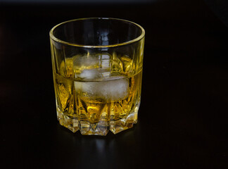 A glass of whiskey with ice on a black background. Copy the space.