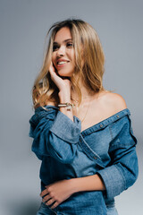 Fototapeta premium seductive, smiling woman in denim shirt, with naked shoulder, looking away isolated on grey