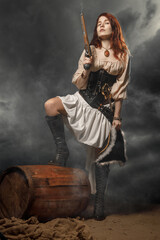 Young pirate female with long red hair. Woman is wearing a black corset bustier, tricorn hat , gun belt and armed with a pistol and sword. - 398266731