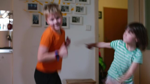 Cheerful children dance in the room in the evening in self-isolation. Move bodies vigorously, jump. Children's party at home.