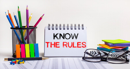On the table are colored pencils in a stand, brightly colored stickers, glasses and a notebook with the inscription KNOW THE RULES. Motivating concept. Call to action
