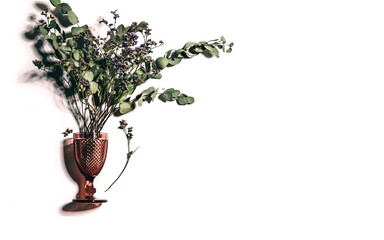Dried flowers and green leaves bouquet inside red wine glass with shadows and space for text, floral background  