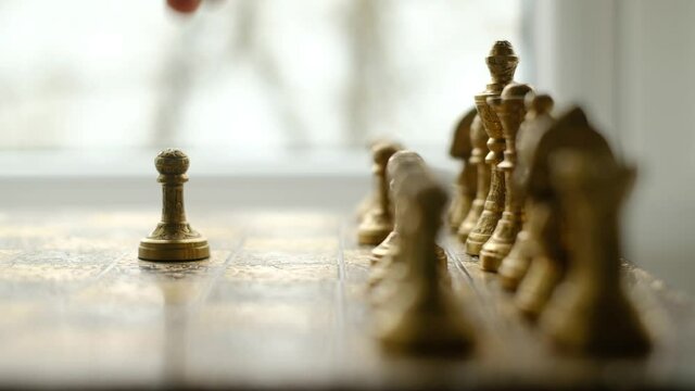 Close-up chess game. Metal chess pieces and the hand of a man who makes the first move with a pawn. The camera moves along the chessboard. UHD 4k video
