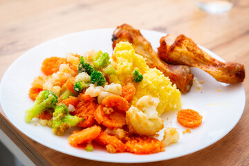 Baked chicken drumsticks with mashed potatoes and vegetables on the plate