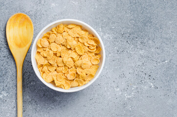 Corn flakes in a plate and a wooden spoon. Healthy breakfast. Copy space