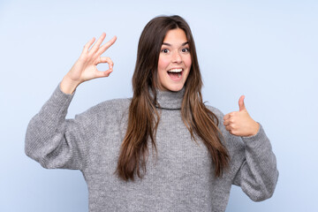 Teenager Brazilian girl over isolated blue background showing ok sign and thumb up gesture