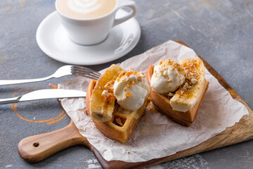 belgian waffle with ice cream and banana and cup of coffee on gray table