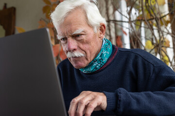 Portrait of a senior man, working on his laptop in the outdoor lounge, looking at the camera.