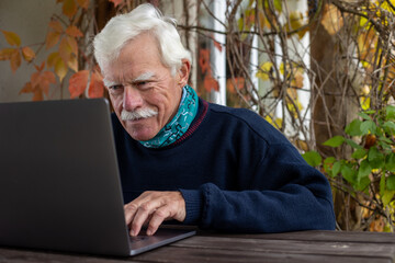 Portrait of a smiling senior man, working on his laptop in the outdoor lounge, looking at the camera.