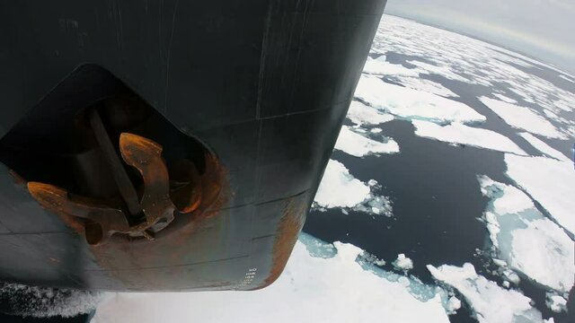 The bow of icebreaker with anchor splits the ice. Black bow of the ship. Rusty anchor on Board. The ship is moving through the blue ice. Slow Motion. Close up.
