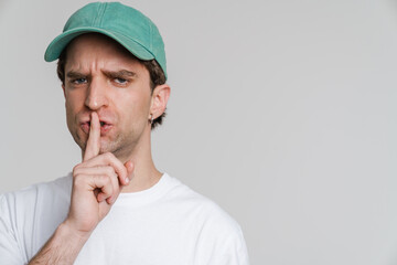 Young irritated man in cap showing silence gesture on camera