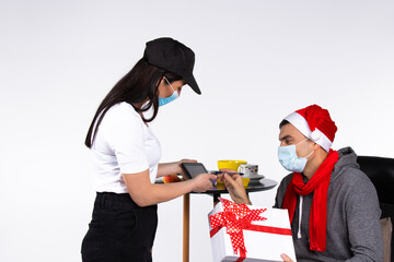 A woman courier delivers a Christmas order wearing a medical mask. The concept of courier delivery during a pandemic.