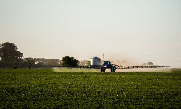 fumigadora fumigando un campo de soja con un silo de fondo 