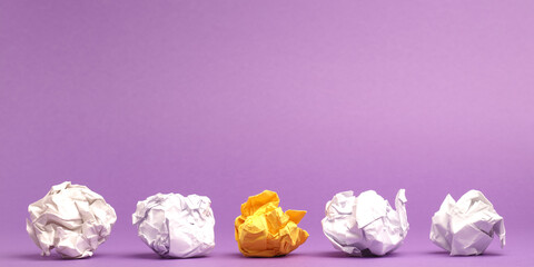 Colorful crumpled paper balls in a row on a purple studio background