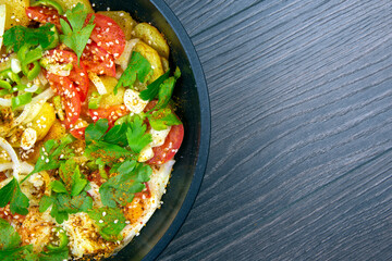 cooked fried omelet with herbs, spices and vegetables in a black pan on a wooden table