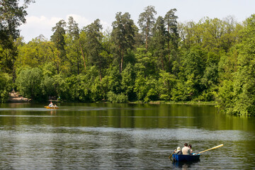 Fototapeta na wymiar People float by boat on the lake in the famous Pushcha Vodytsya park in Kyiv, Ukraine. May 2011