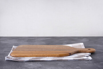 Wooden kitchen board with a kitchen towel on a gray background, space for text.