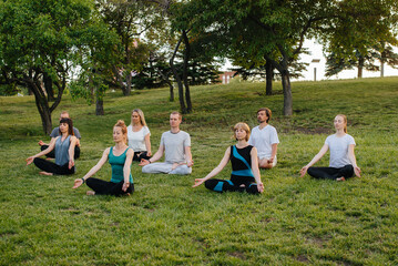 Naklejka na ściany i meble A group of people do yoga in the Park at sunset. Healthy lifestyle, meditation and Wellness