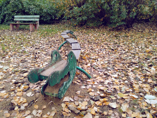 Old shabby wooden alligator for kids activity on autumn playground covered with fallen leaves