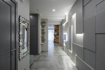 Contemporary light interior of luxury flat. Modern design of wall with lamps. Logs on shelves. Mirror on wall.