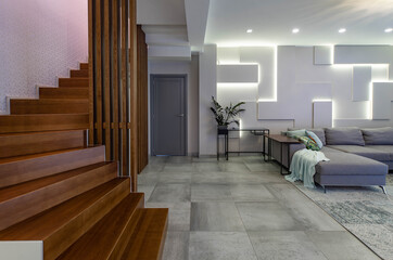 Contemporary interior of luxury apartment. Spacious living room with furniture. Modern design of wall. Wooden staircase.