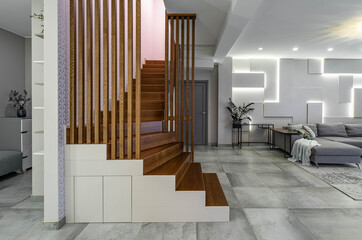Contemporary interior of luxury apartment. Spacious living room with furniture. Modern design of wall. Wooden staircase.