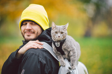 Portrait of tall young Caucasian happy man outdoor playing with gray funny handsome kitten sits on...