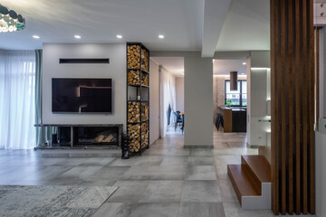 Modern interior of luxury apartment. TV on wall. Logs for fireplace. Wooden staircase.