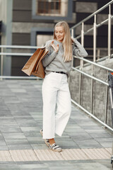 Woman in a summer city. Lady with brown bags. Woman in a gray sweater.