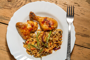 Baked chicken drumsticks and wings marinated with risotto in a plate on the table next to a fork.