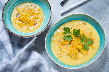 Turquoise bowls with gazpacho cold soup made of sweet corn, high angle view on a light-blue stone background, horizontal shot