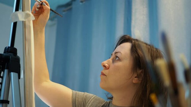 a young woman paints a picture on an easel.