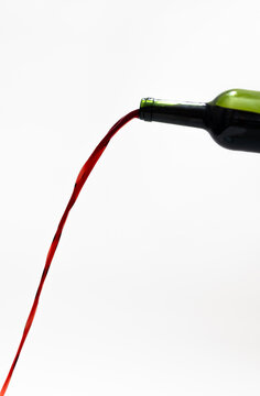 Red wine pouring out of a bottle with long stream on white background